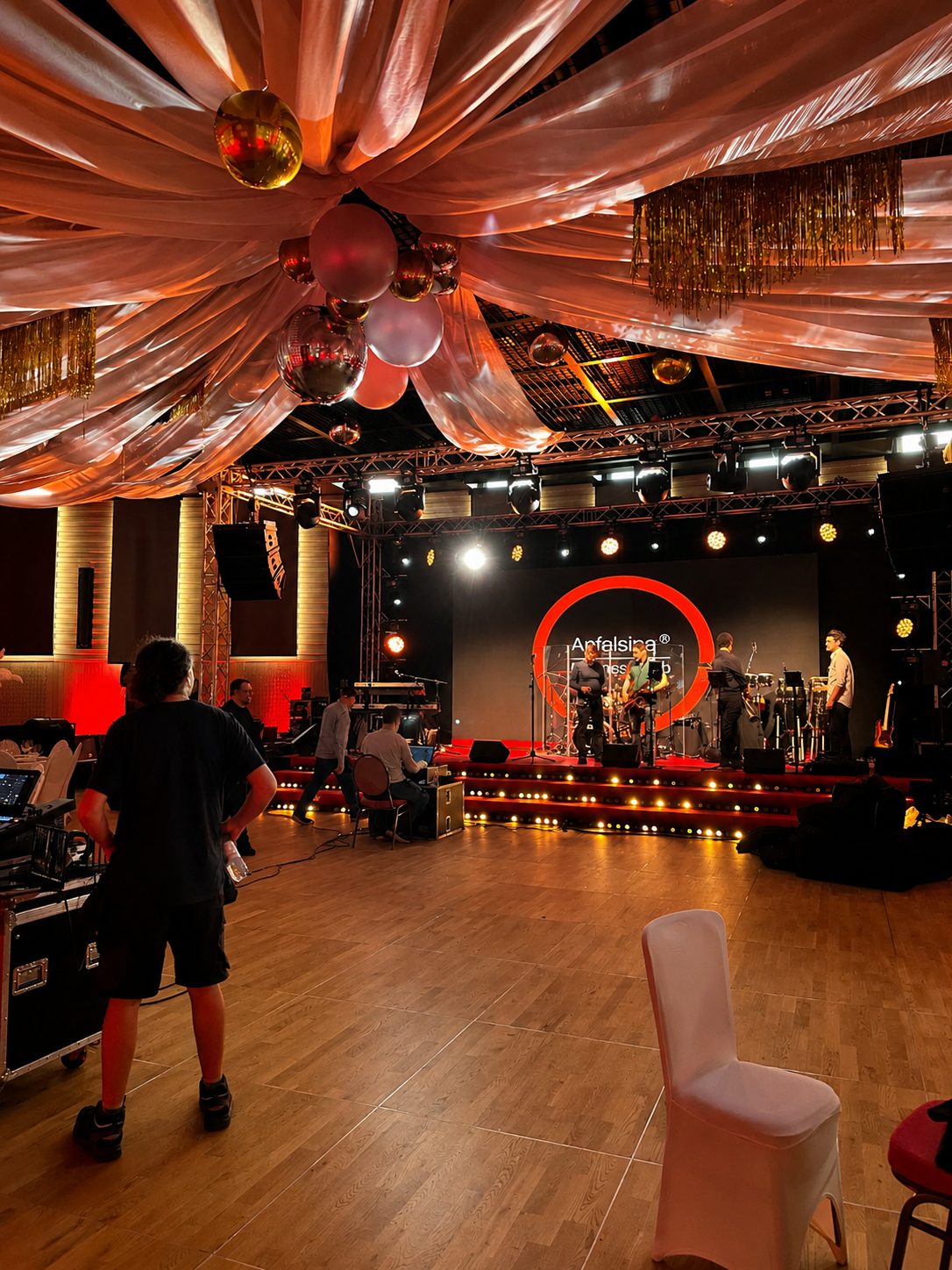 Live-Band spielt auf rot beleuchteter Bühne unter drapiertem Stoff und hängenden Discokugeln