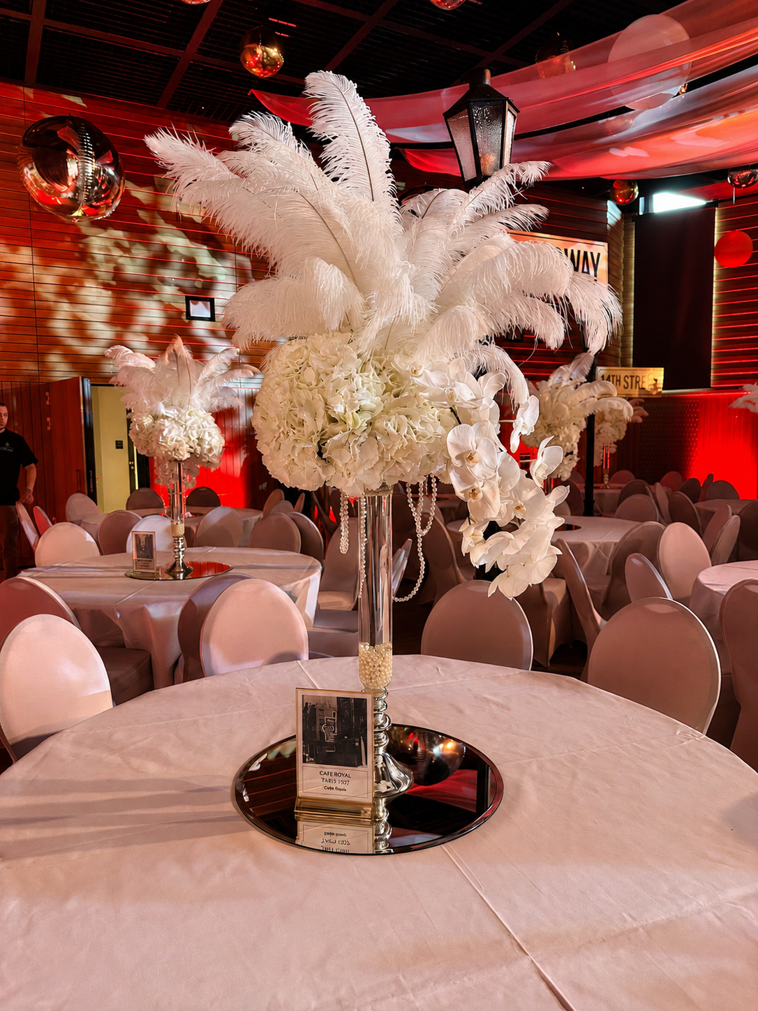 Detail des Federn-Centerpieces mit Perlensträngen und Vintage-Fotokärtchen auf dem Tisch