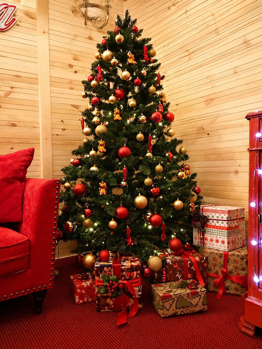 Geschmückter Weihnachtsbaum mit rot-goldenem Schmuck und Geschenken in der Hütte