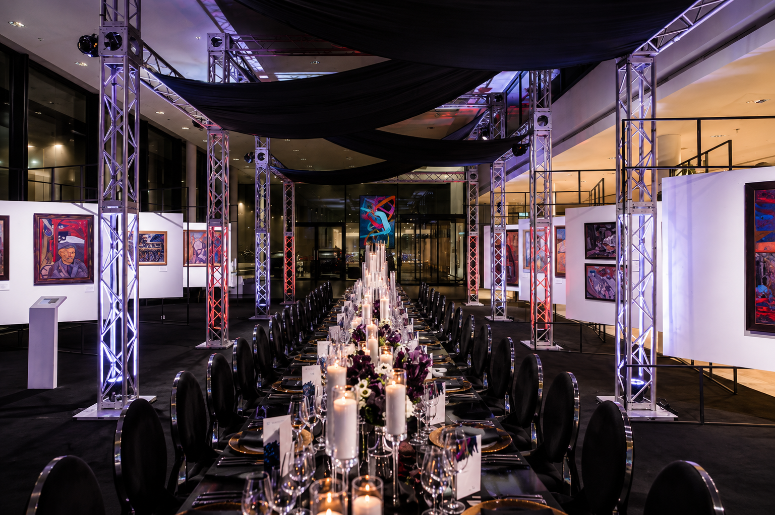 Schwarz drapierter Gala-Dinner-Aufbau mit kerzenbeleuchtetem Blumen-Centerpiece über die gesamte Raumlänge